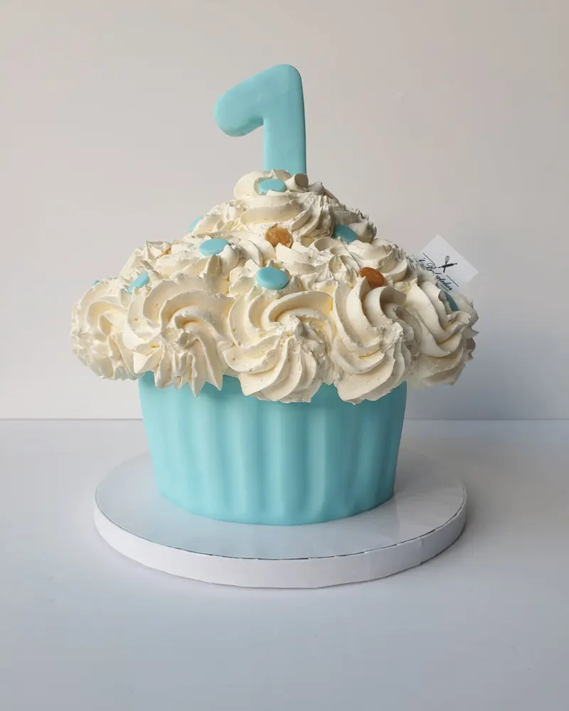 Lichtblauwe reuzecupcake-taart met witte rozetten en een cijfer 1